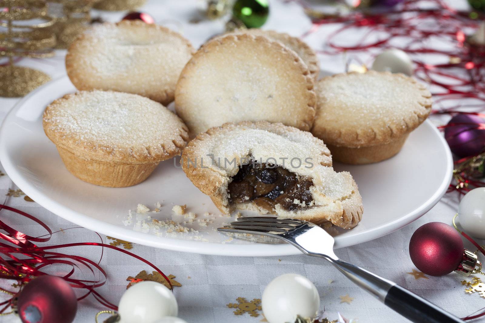 Mince pies on a plate surrounded by holiday decorations.