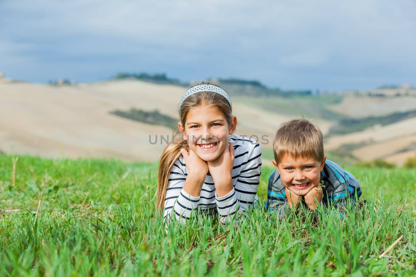 Happy sister and brother having fun on vacations in Tuscan against beautiful landscape background