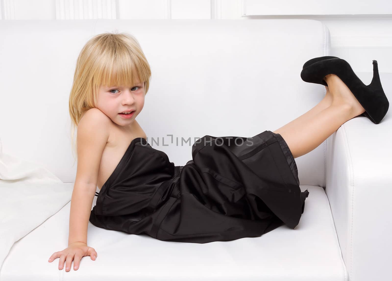 Girl 3 years old in her mother's high heels sitting on a white sofa