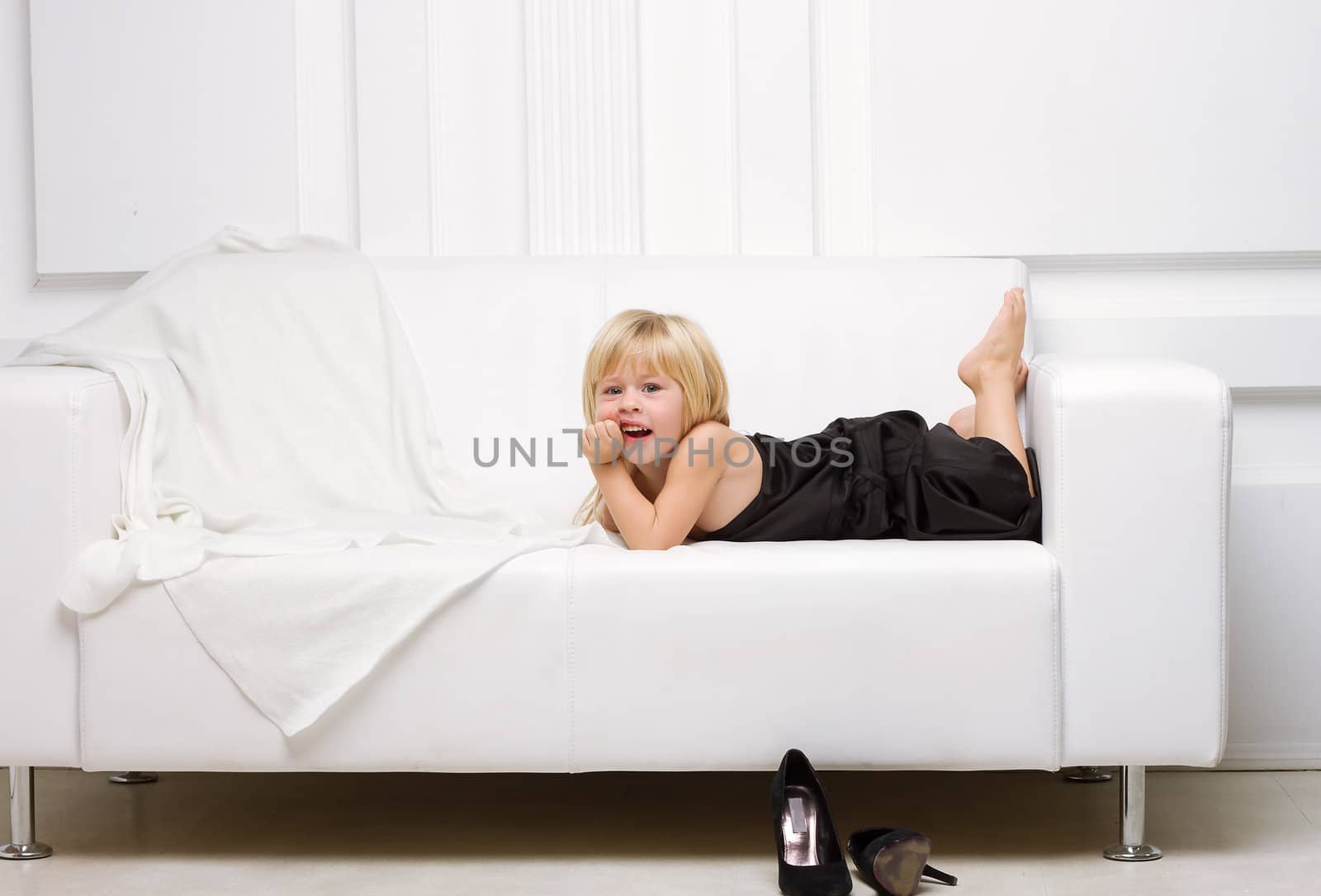 3 years old girl lying on a white sofa in my mother's dress, standing next high heels