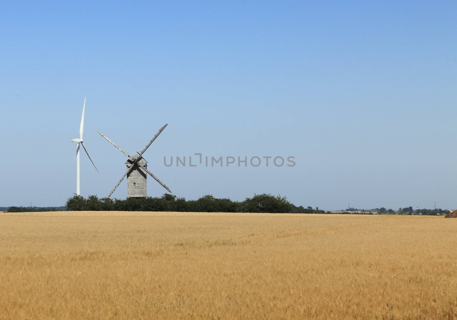 Image of a traditional windmill close to a modern eolian turbine in a cereal field.