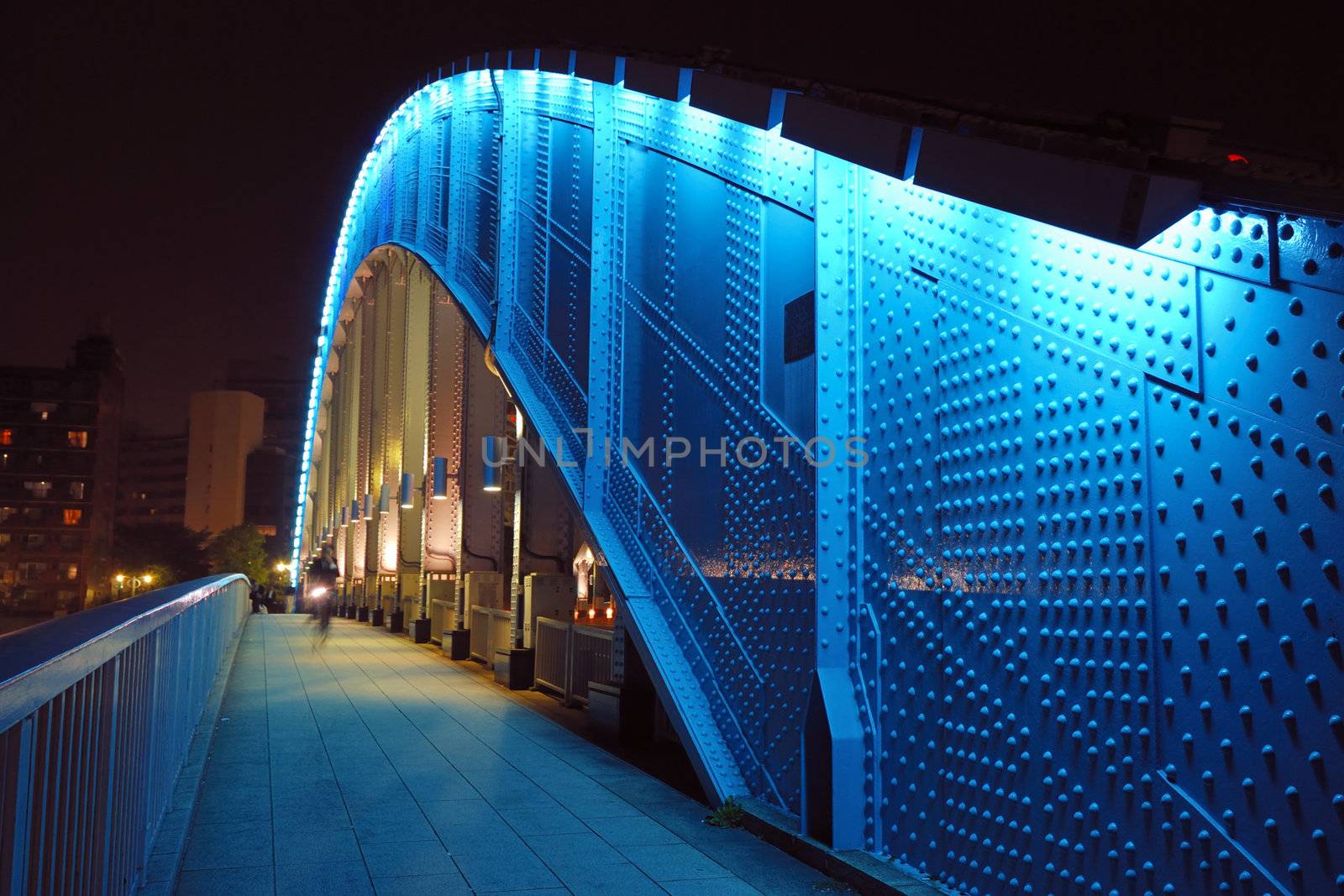pedestrian way along the metallic arc structure of Eitai bridge with moving bicycle by night time in Tokyo Japan; focus on metallic structure