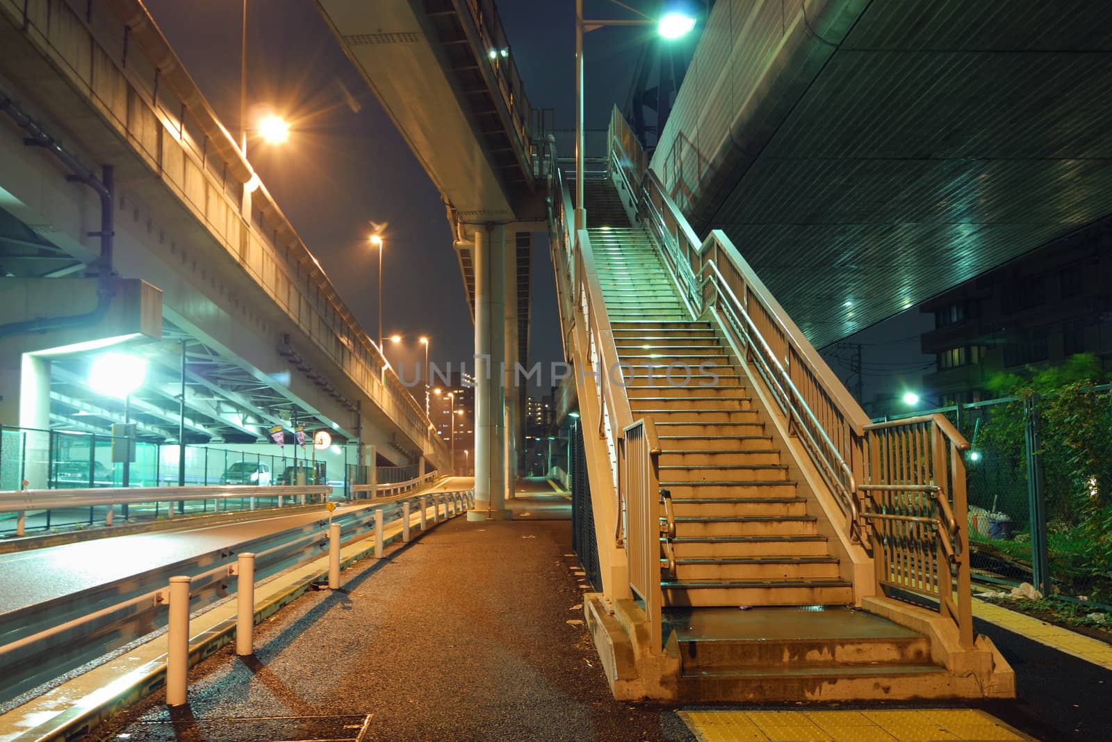 illuminated stairs going up between huge highway structures in night city