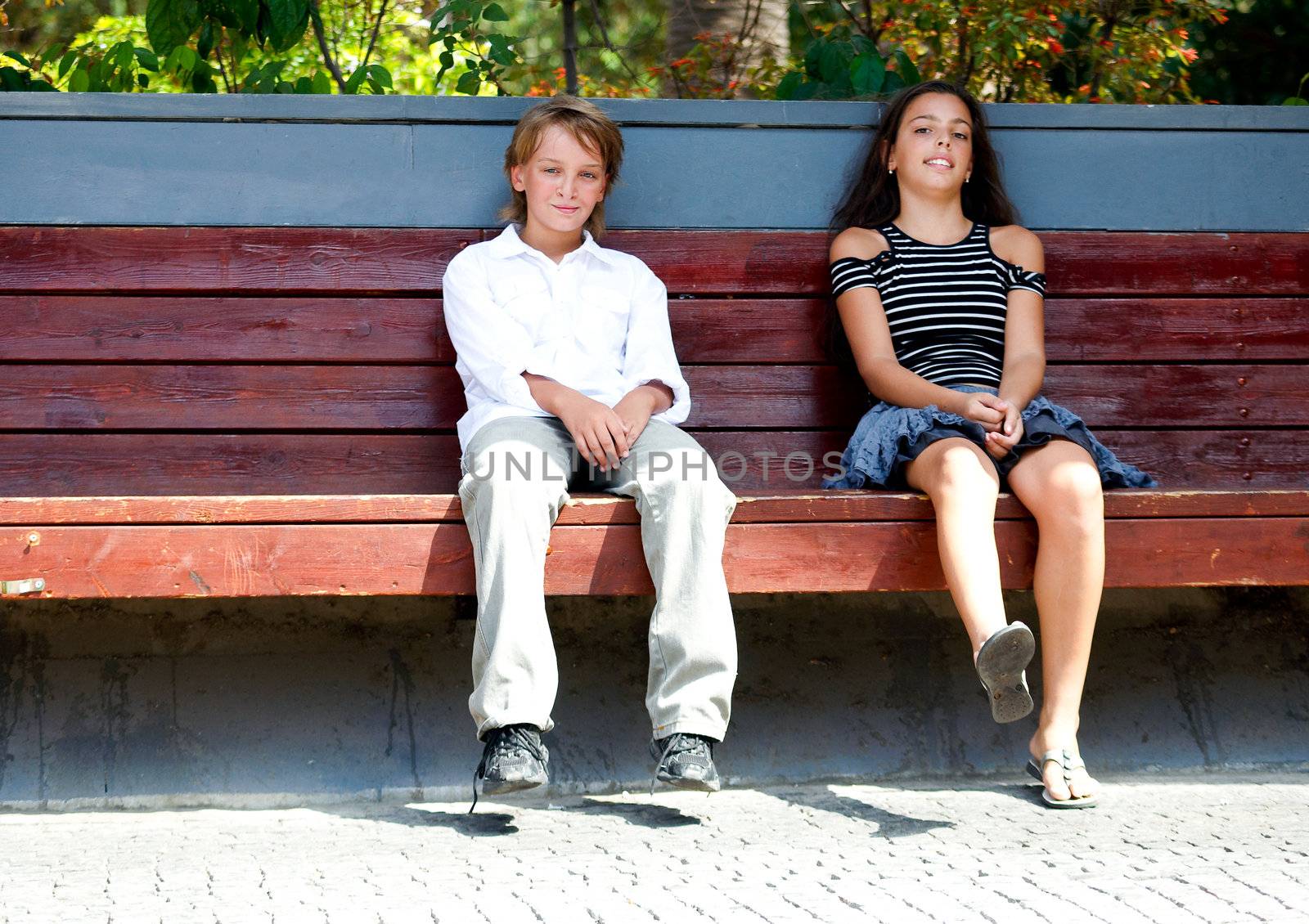 Boy and girl sitting on the bench. by LarisaP