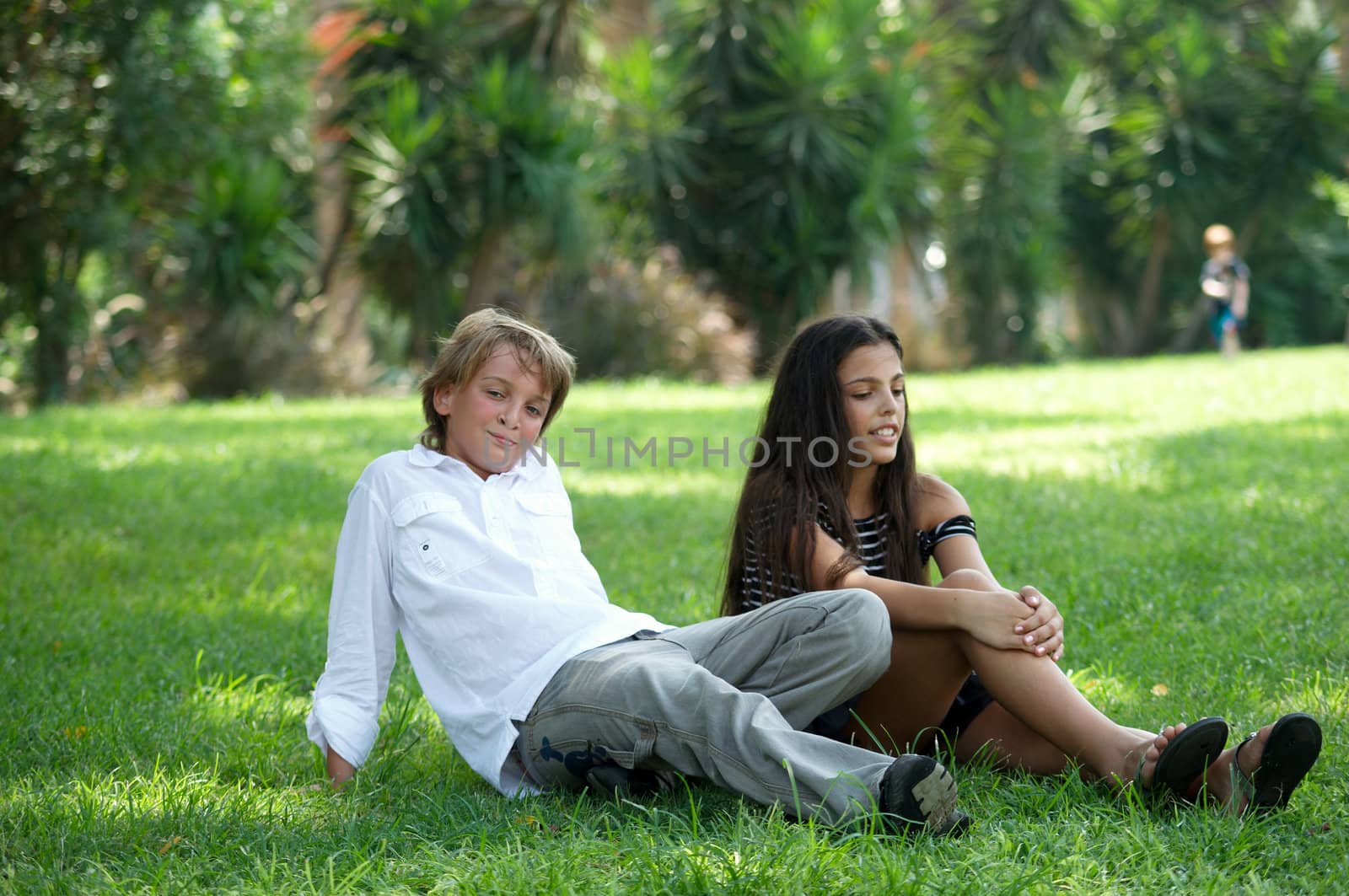 Pre-teen boy and girl in a bright sunny summer day sitting on the grass in the park.
