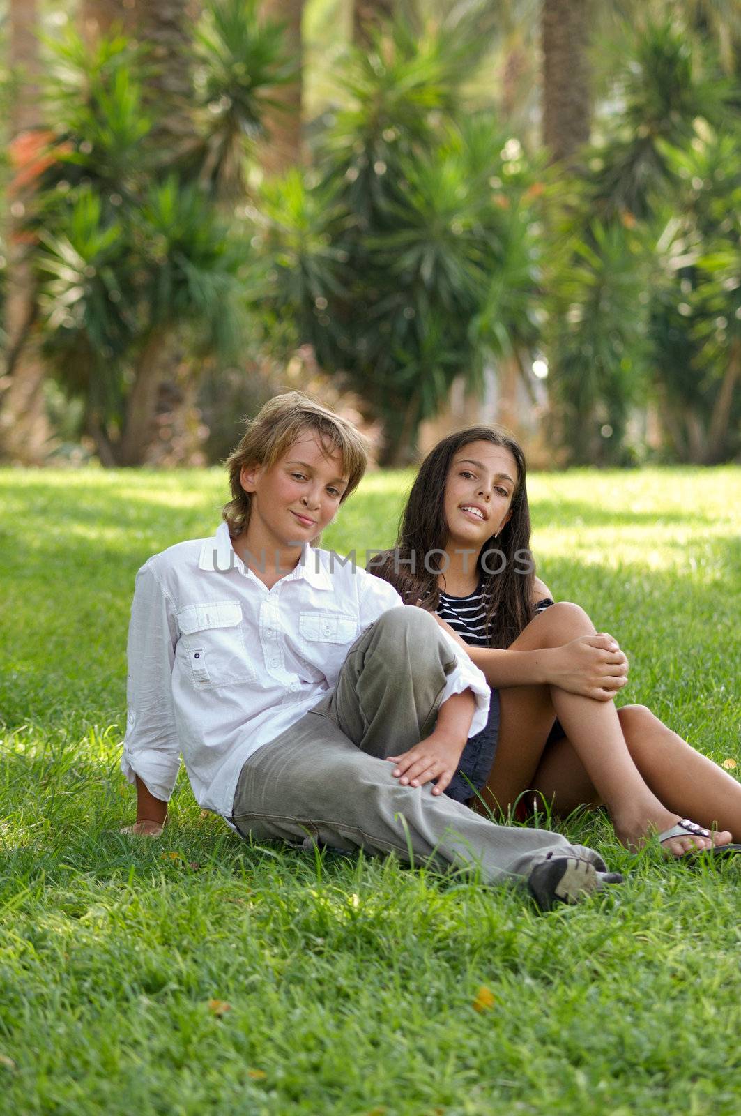Pre-teen boy and girl in a bright sunny summer day sitting on the grass in the park.