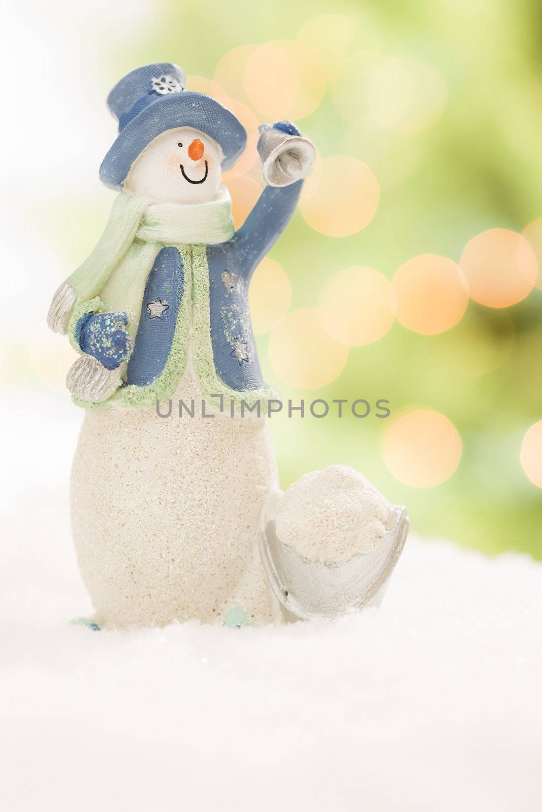 Snowman Statue On Snow Over a Blurry Abstract Green and Gold Background.