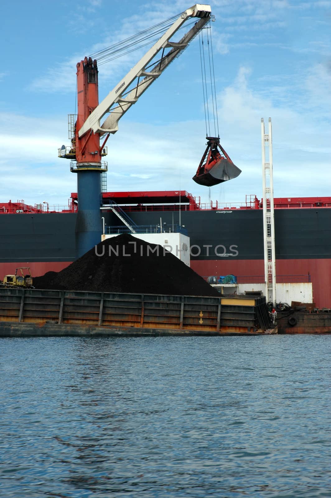 coal is being loaded onto tankers with  crane from a pontoon