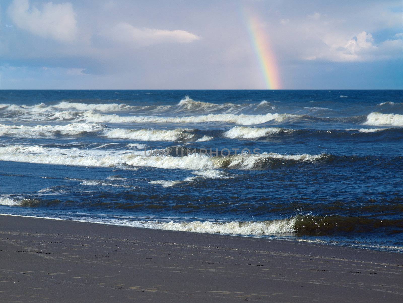 Ocean Waves Breaking on Shore with a Partial Rainbow in the Background