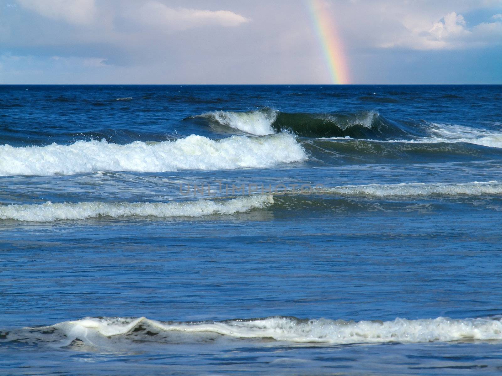 Ocean Waves Breaking on Shore with a Partial Rainbow in the Background