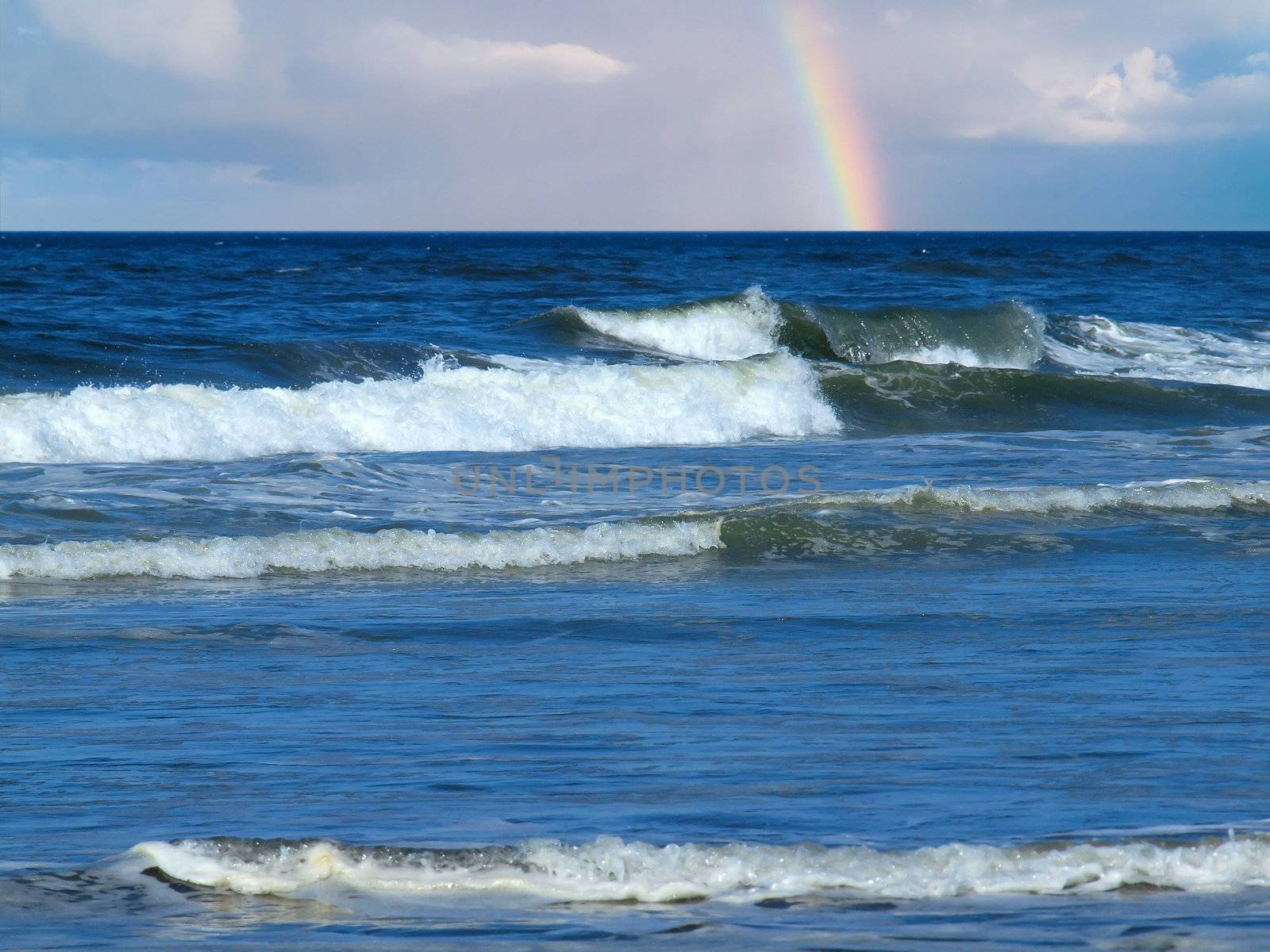 Ocean Waves Breaking on Shore with a Partial Rainbow in the Background by Frankljunior