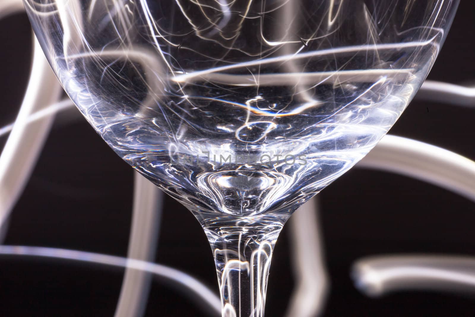 Abstract light tracks behind drinking glass on black