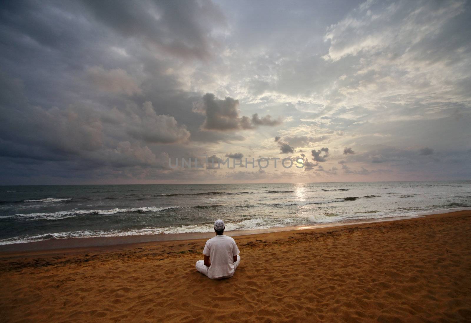 Guy meditating at sunset sitting on coastline 