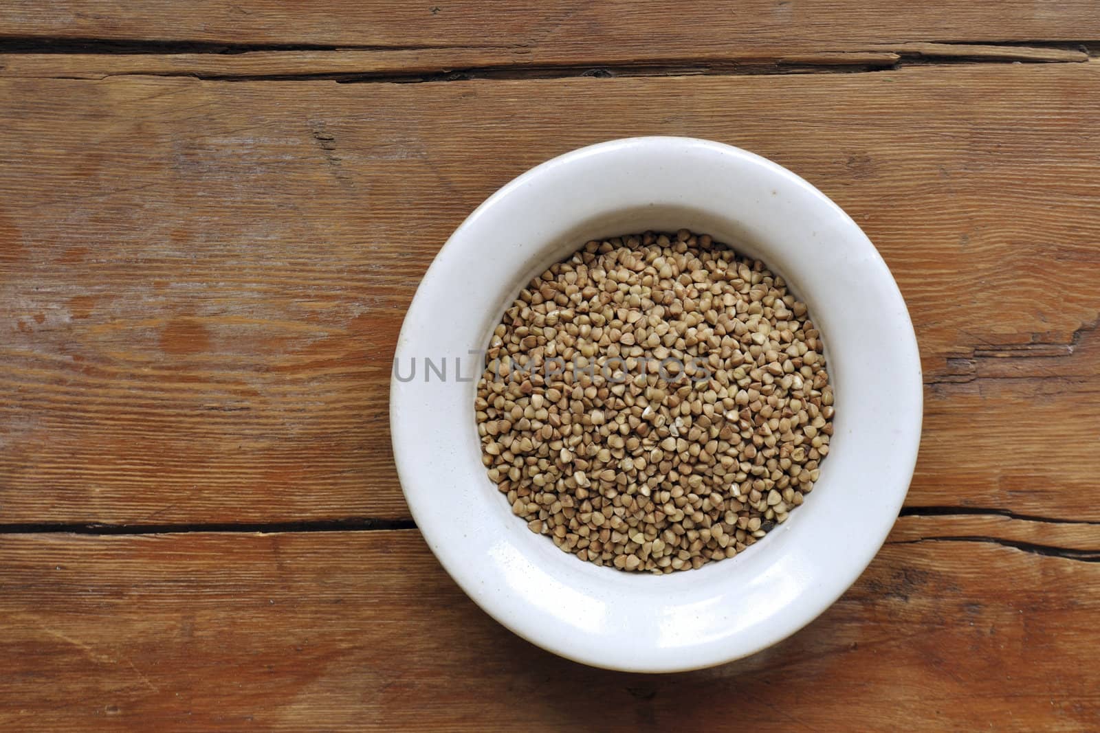 buckwheat grains in white bowl over vintage wooden table background