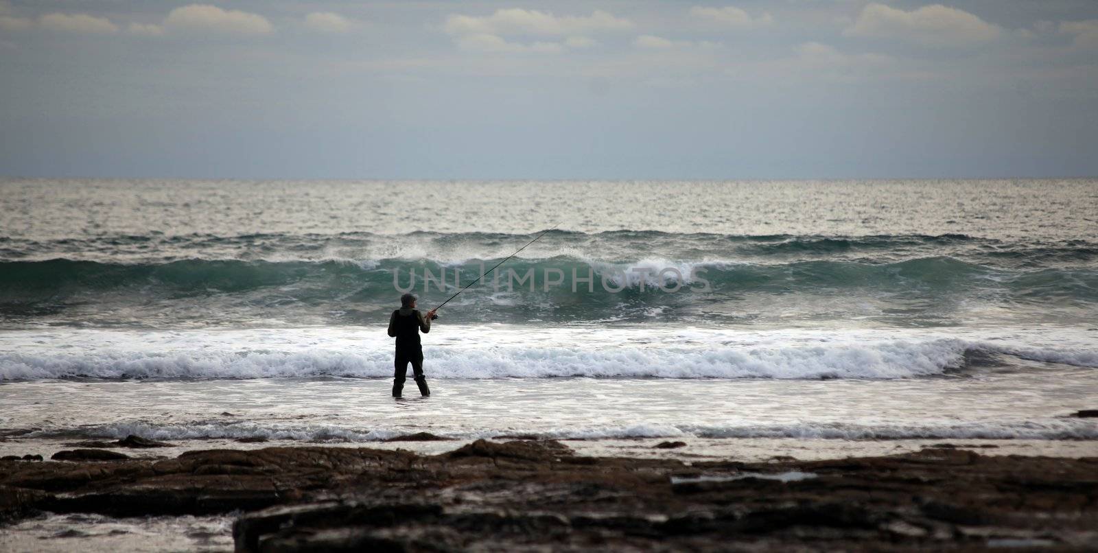 Fisherman sea fishing in surf on dorset coast