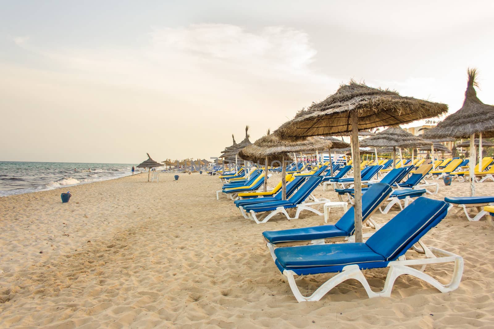 Hammamet beach with shades made of straw, blue beach chairs and beautiful white sand along the coast of the Mediterranean sea