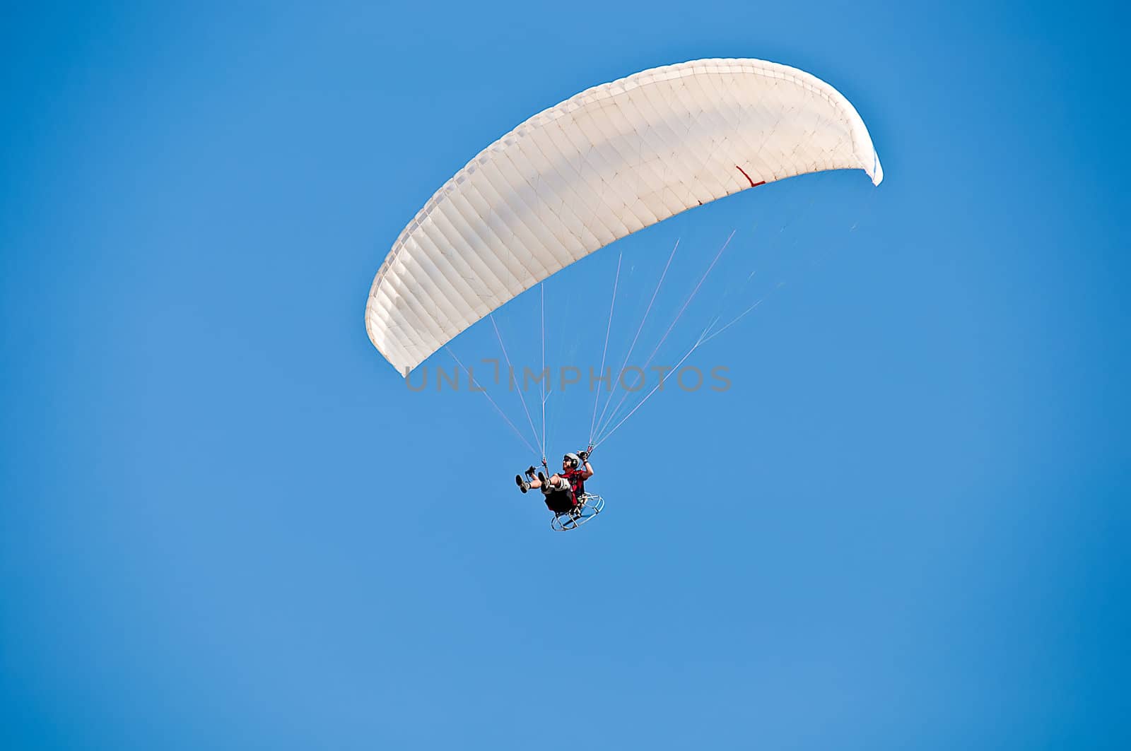 White hang glider in sky over blue sea .