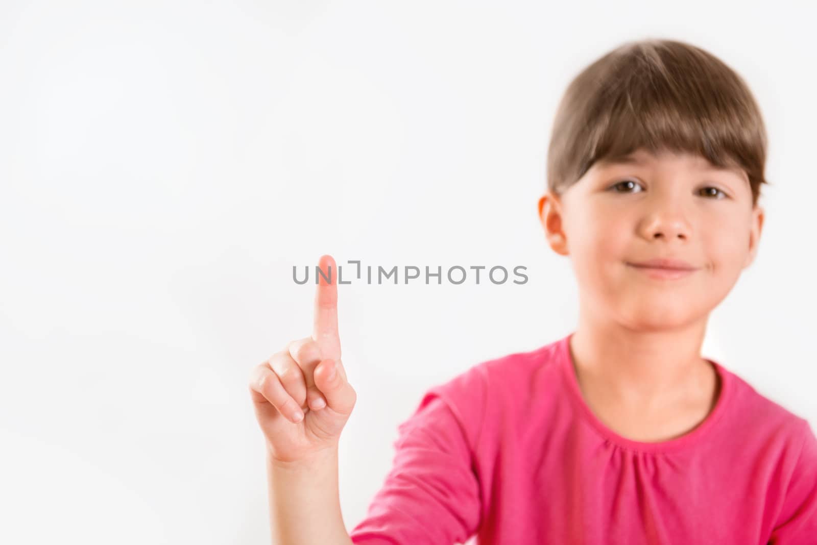 Cute little girl (5-6 year) pointing on copy space or touching virtual screen. Isolated on light gray.