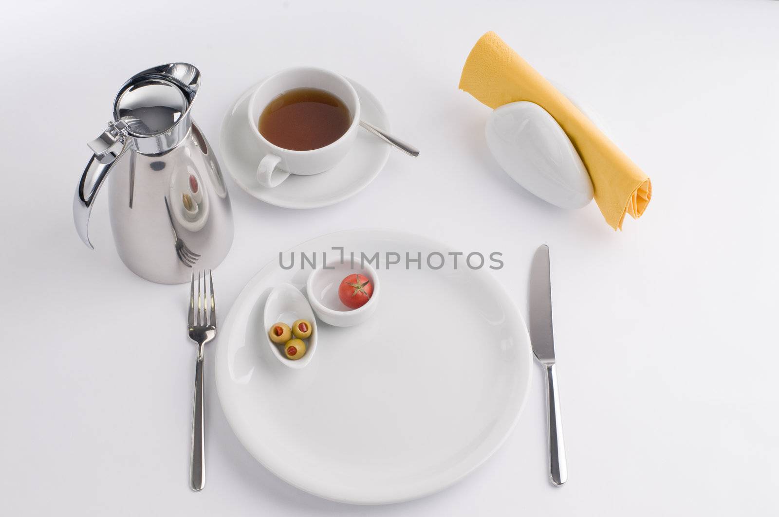 Breakfast table with thermos cup and white china, olive, tomato and bread