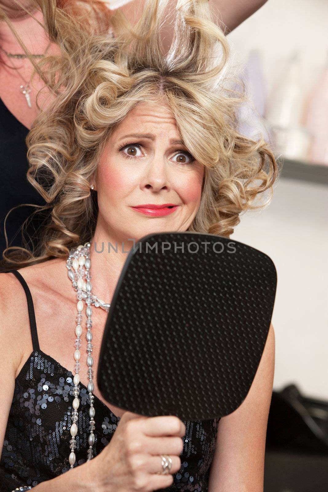 Worried lady holding mirror with stylist working on hair