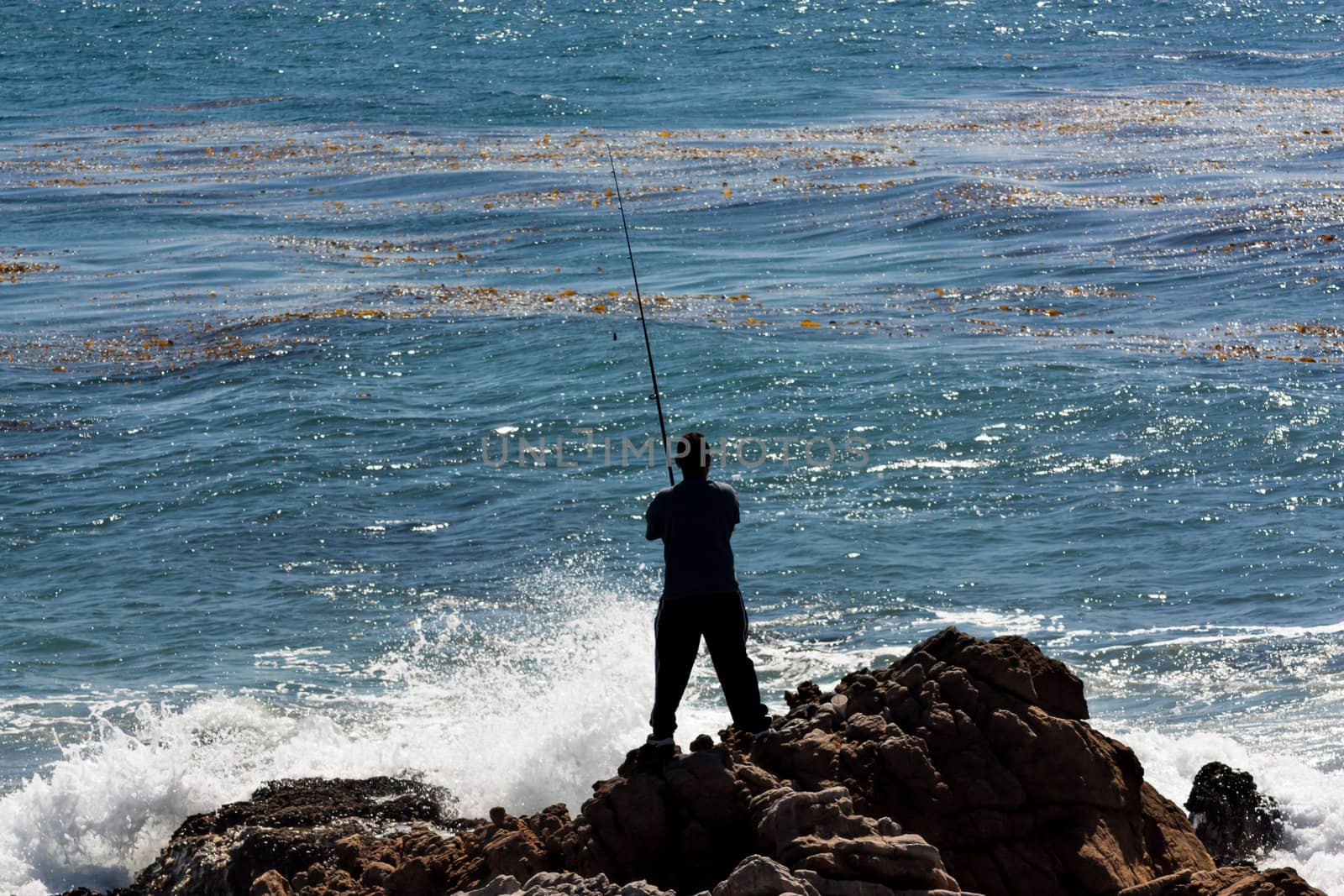 Man Fishes Against the Crashing Ocean Waves by wolterk