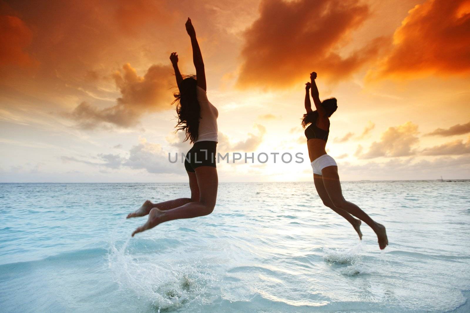 Two happy women jumping on beach by Yellowj