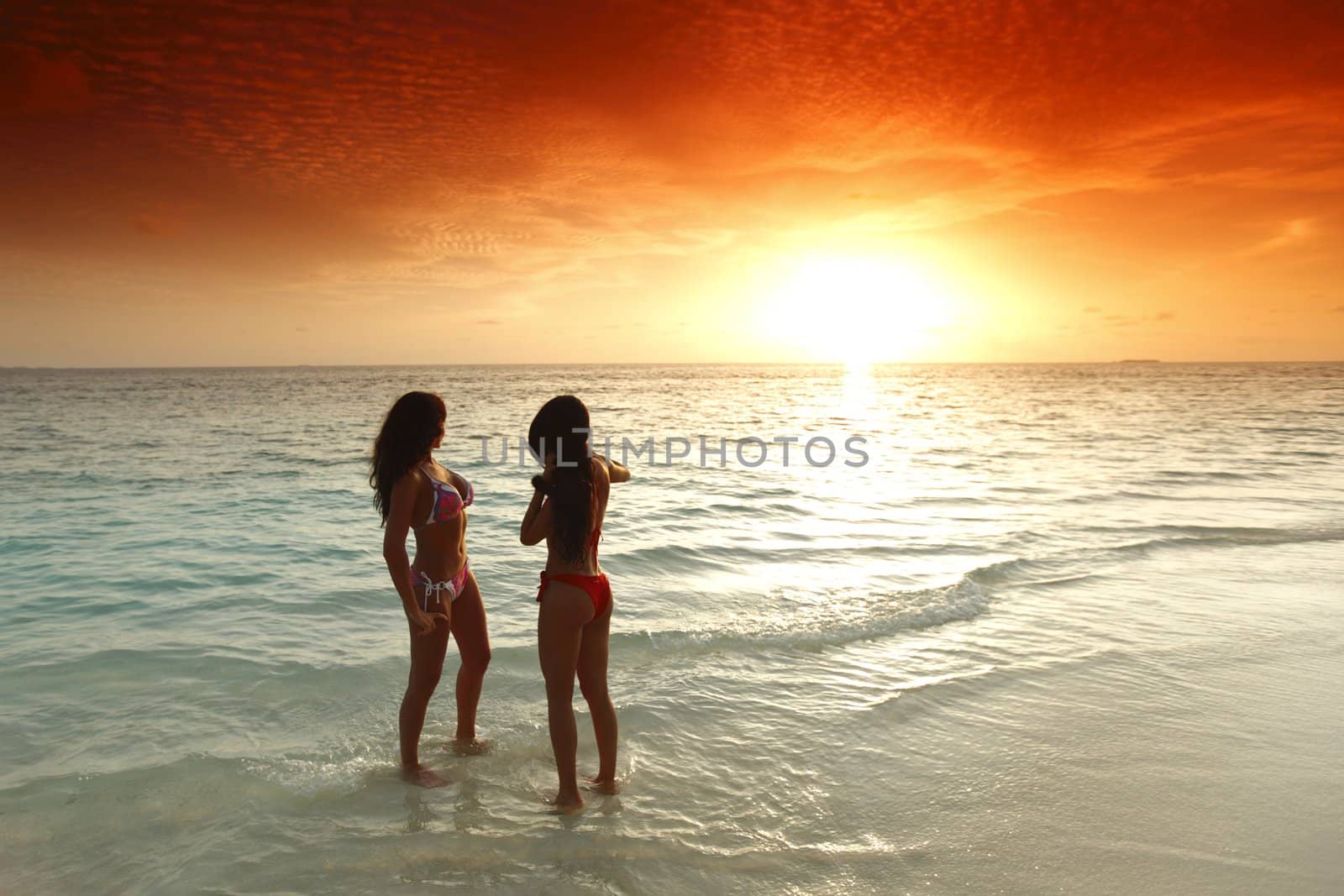 Two women enjoying sunset on beach by Yellowj