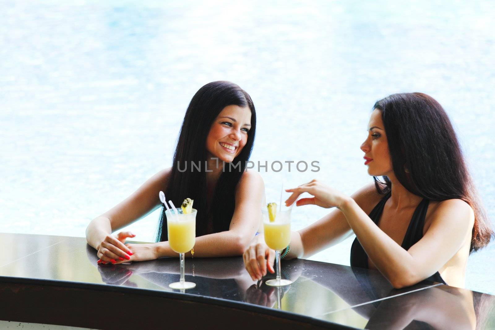 Two beautiful women relaxing in swimming pool with cocktails