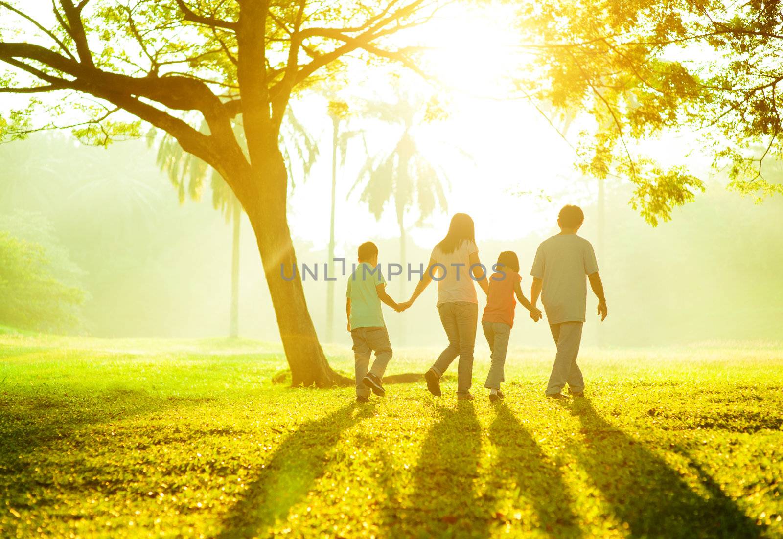 Happy Asian family holding hands walking over green lawn