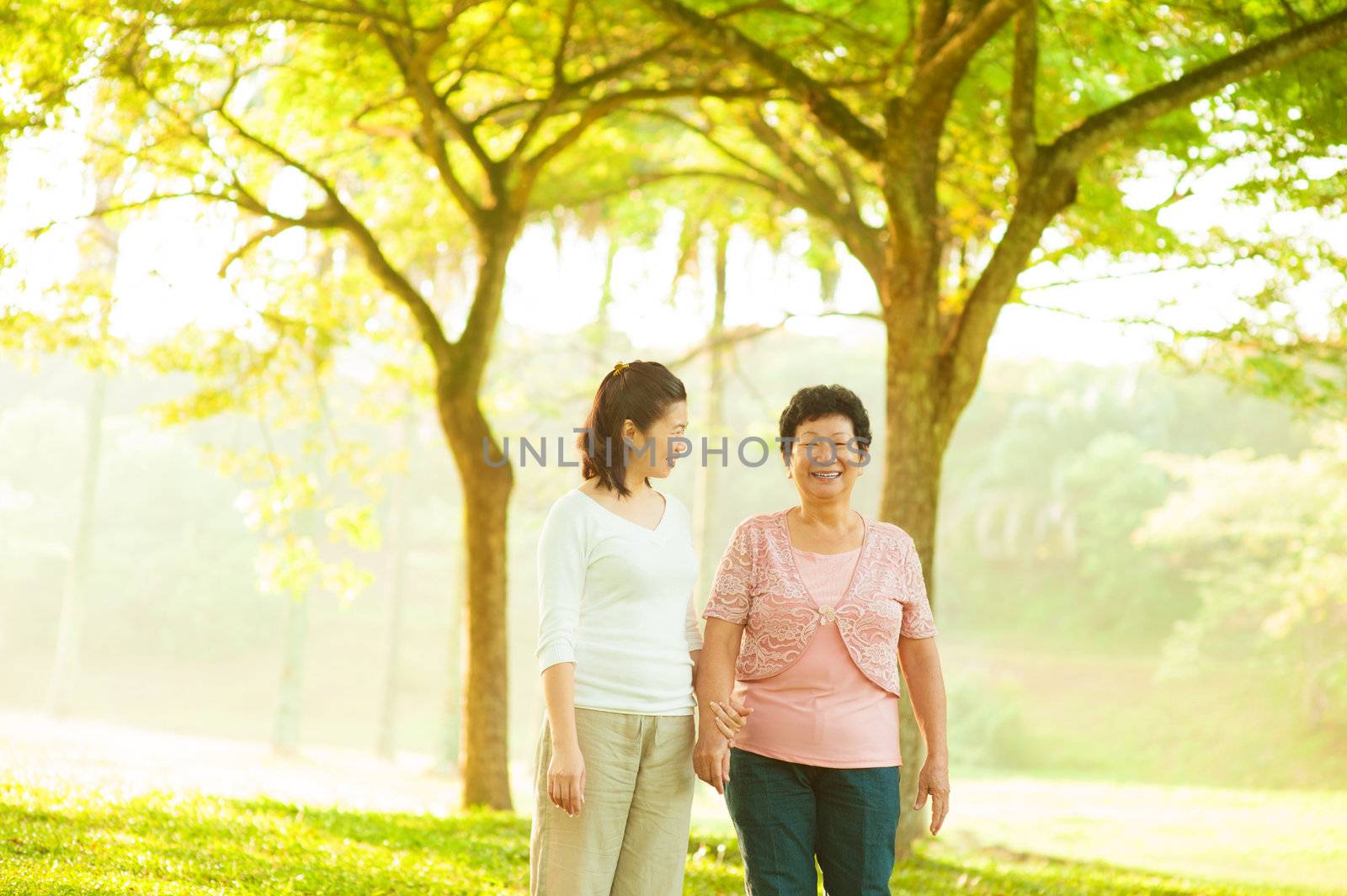 Asian senior mother and adult daughter walking at outdoor green park