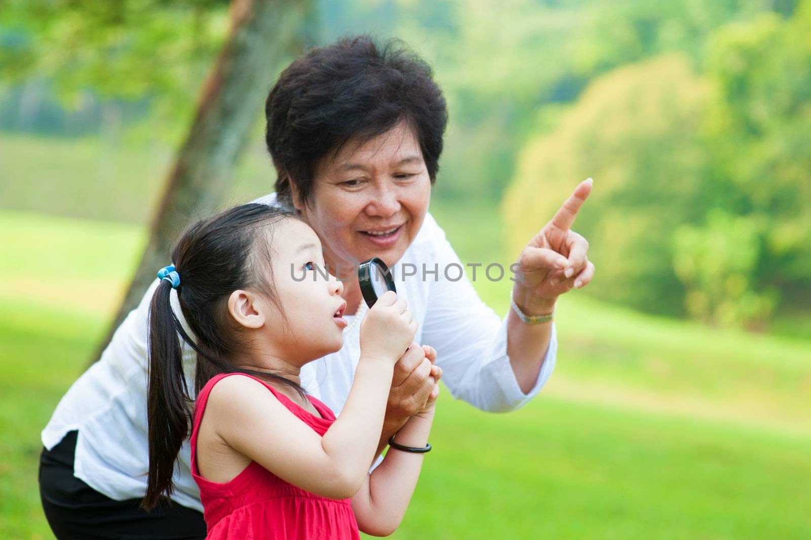 Asian grandmother and granddaughter exploring nature by magnifier
