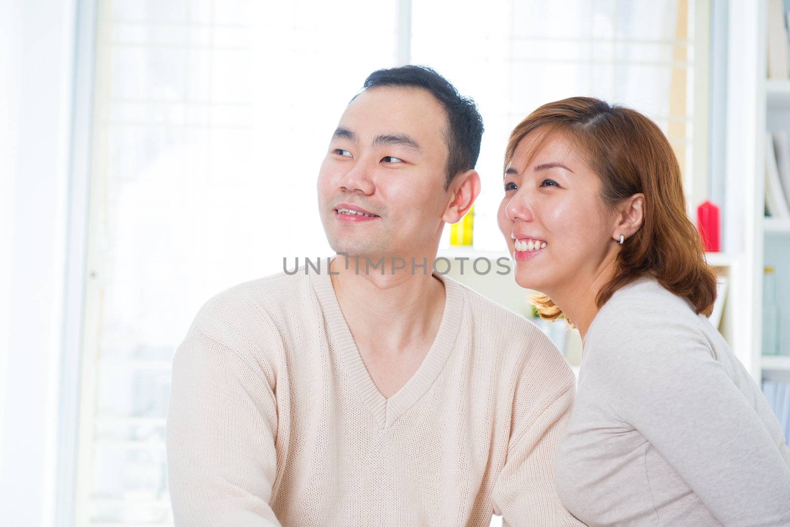 Smiling Asian couple looking away, indoor home
