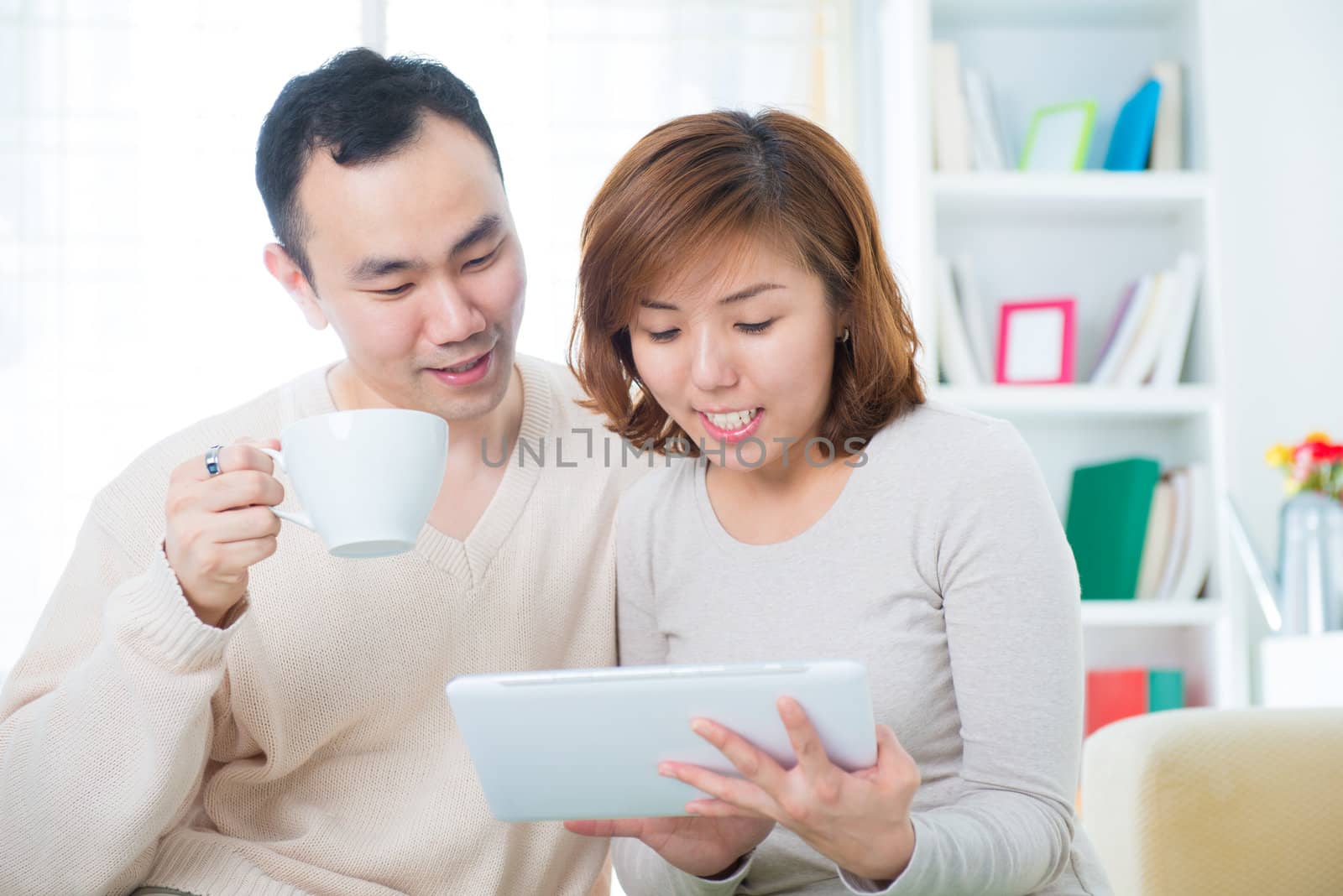 Asian couple drinking tea / coffee and using tablet computer at home