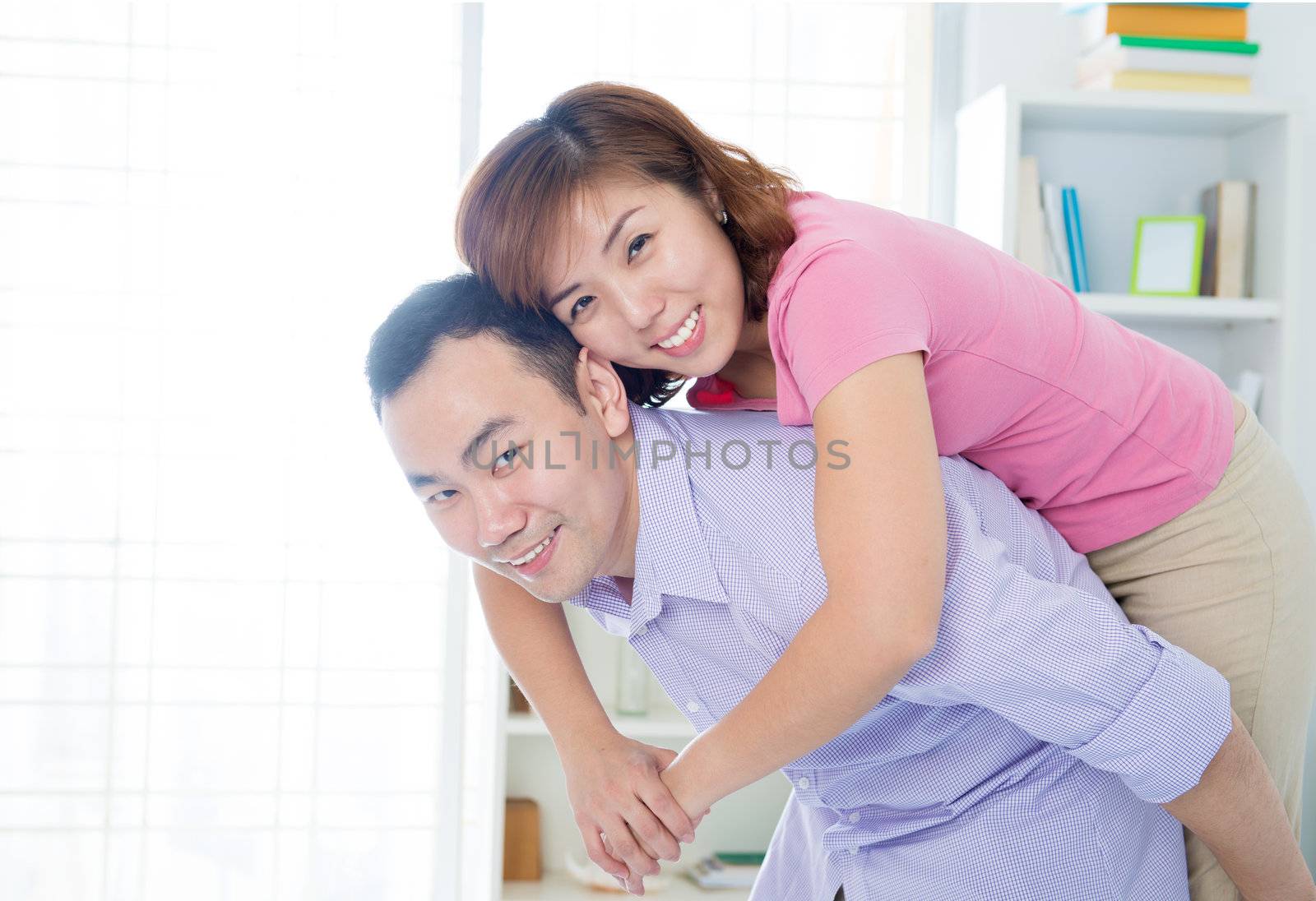 Portrait of a young Asian man giving piggyback to woman indoor.