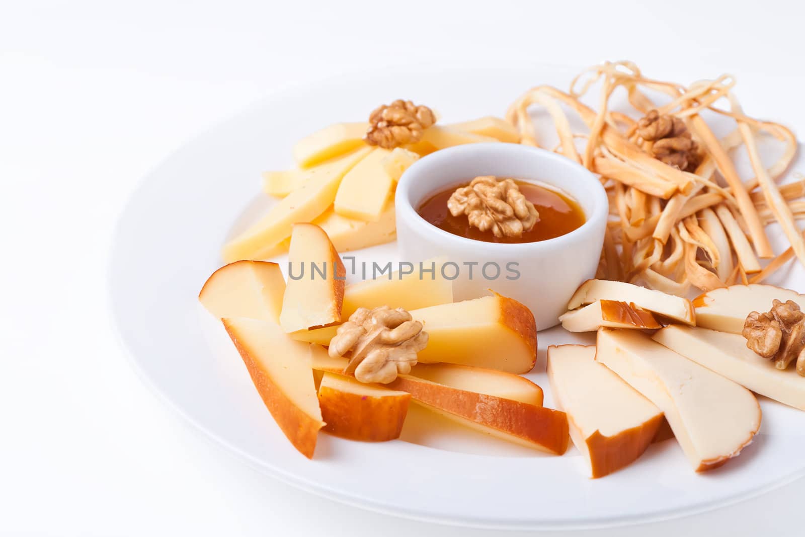 a plate with slices of cheese of different varieties on a white background with nuts and honey