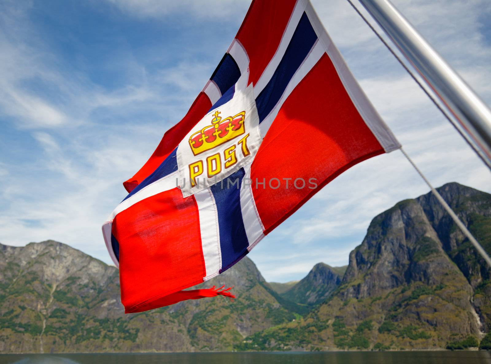 Fluttering Norwegian Post flag against fjord mountains