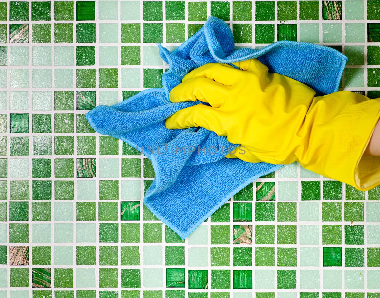 Hand in yellow protective glove cleaning mosaic wall