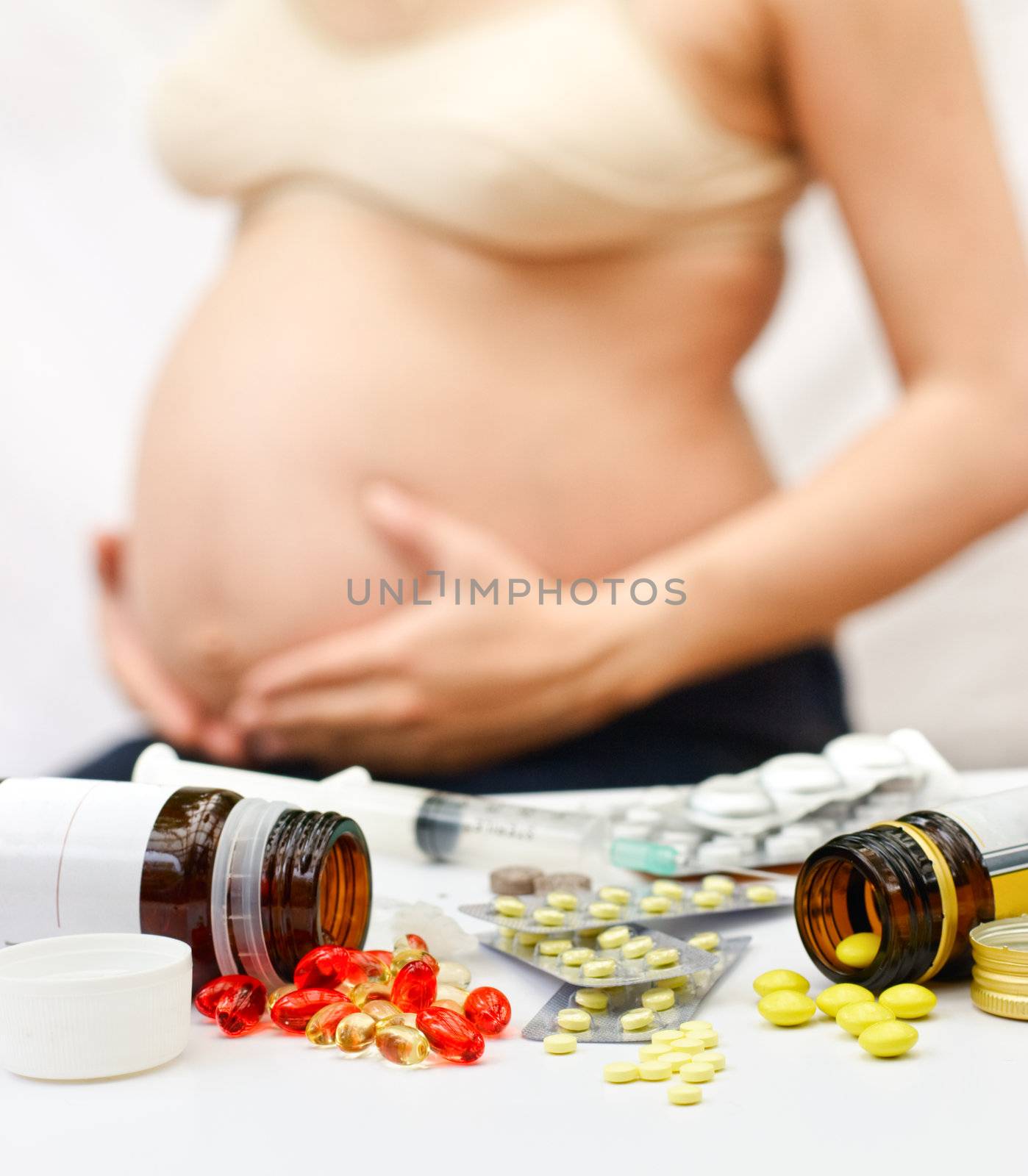 Yellow and red pills spilling from bottles and blisters in front of pregnant woman, shallow DOF