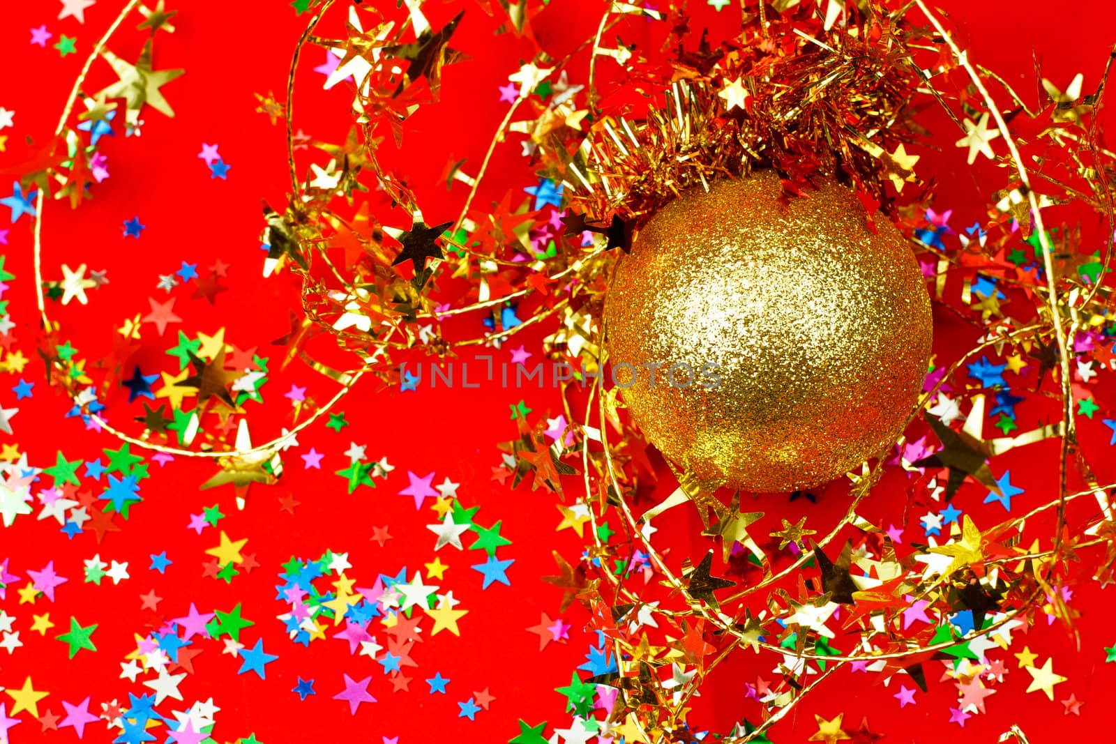 Golden Christmas bauble with star shaped tinsel on red background
