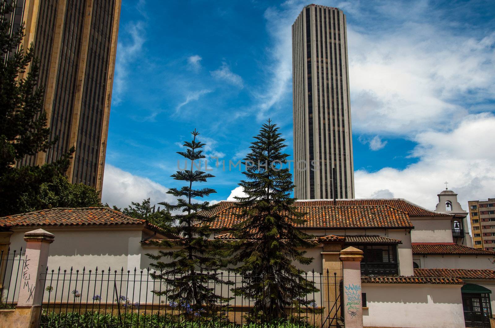 A white colonial church with two skyscrapers rising behind it