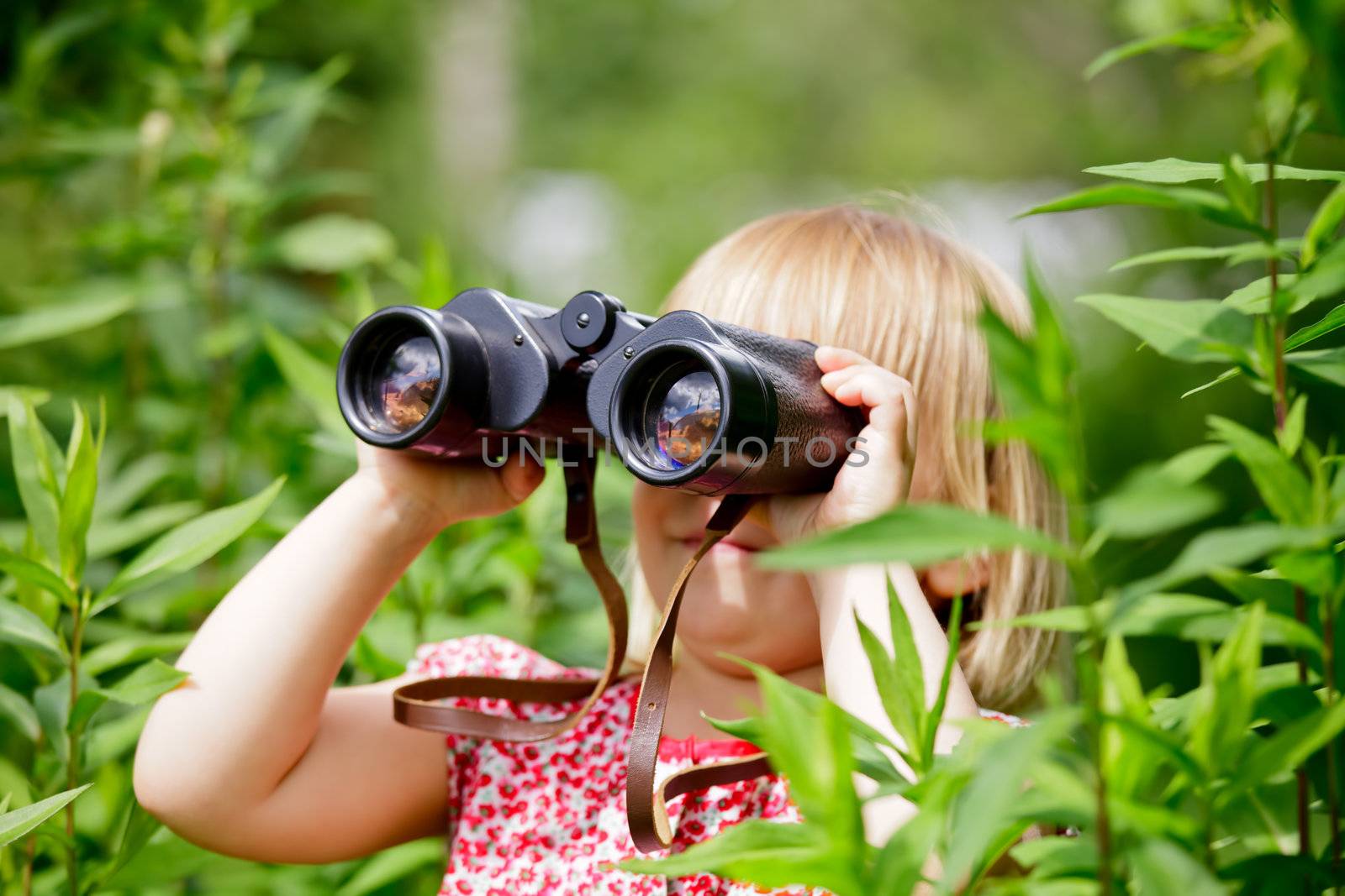 Little girl hiding in grass looking through binoculars outdoor