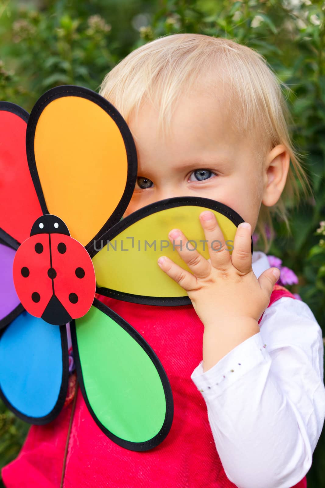 Portrait of cute little girl hiding behind flower toy outdoors
