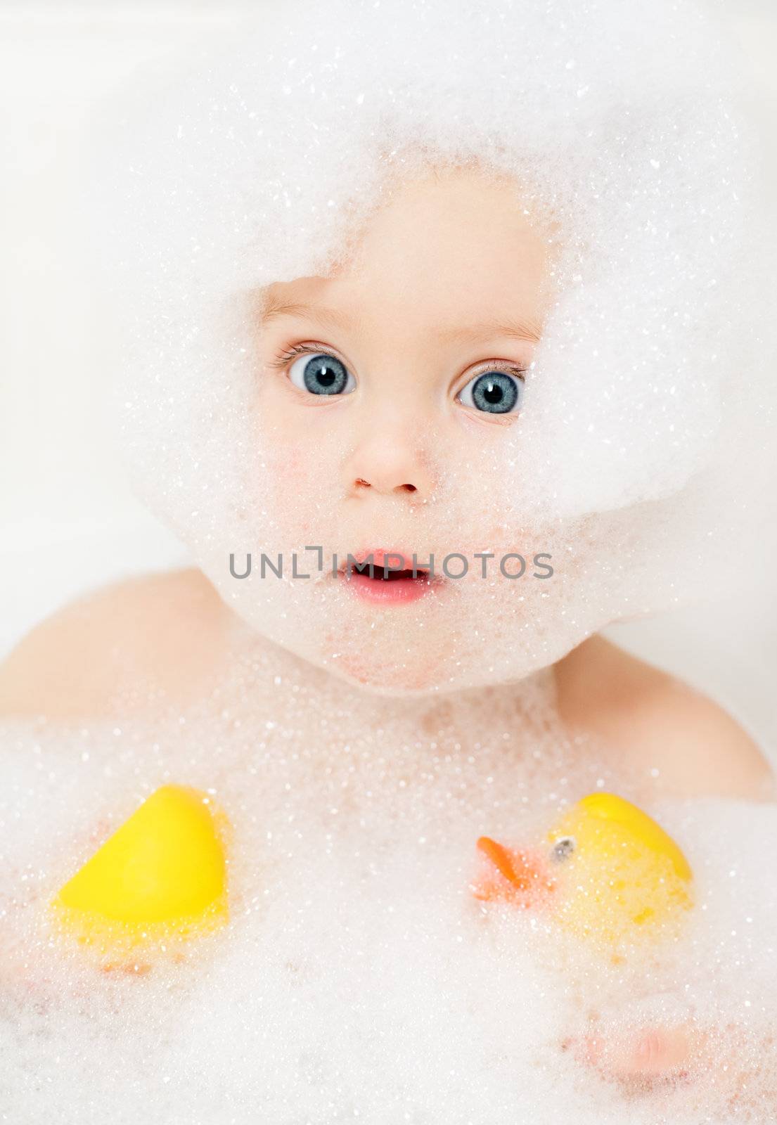 Little baby girl bathing in soapsuds with rubber ducks