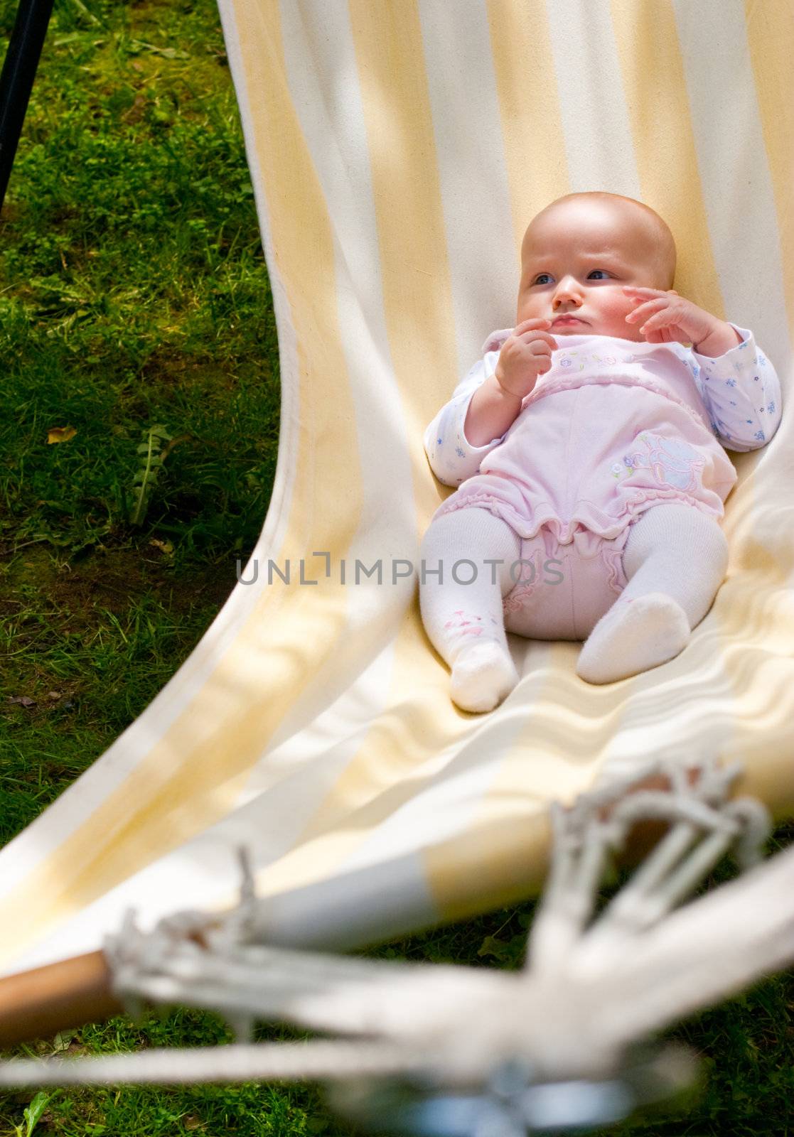 Baby girl in lying in the striped hammock on a summer day