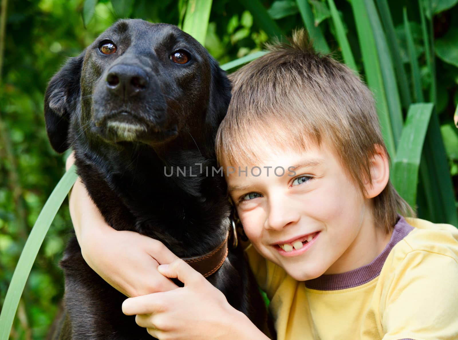 Young boy hugging black dog outdoors