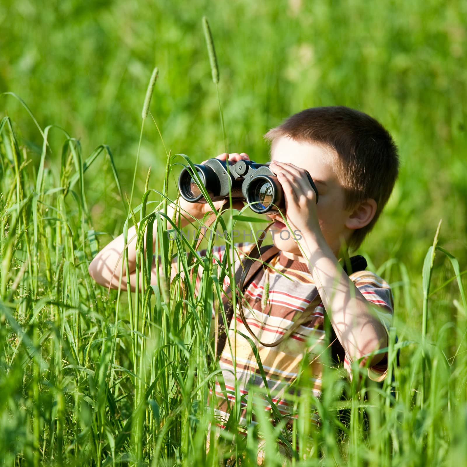 Young boy in a field looking through binoculars