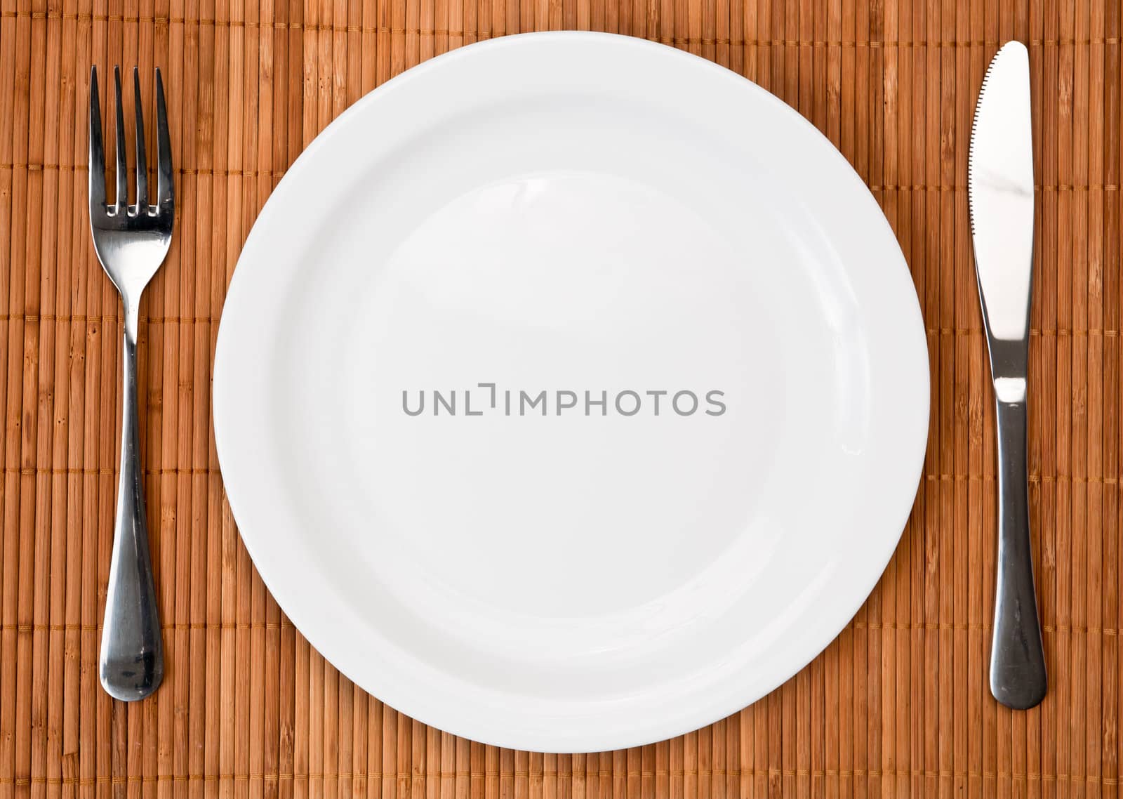 Knife, white plate and fork on bamboo mat