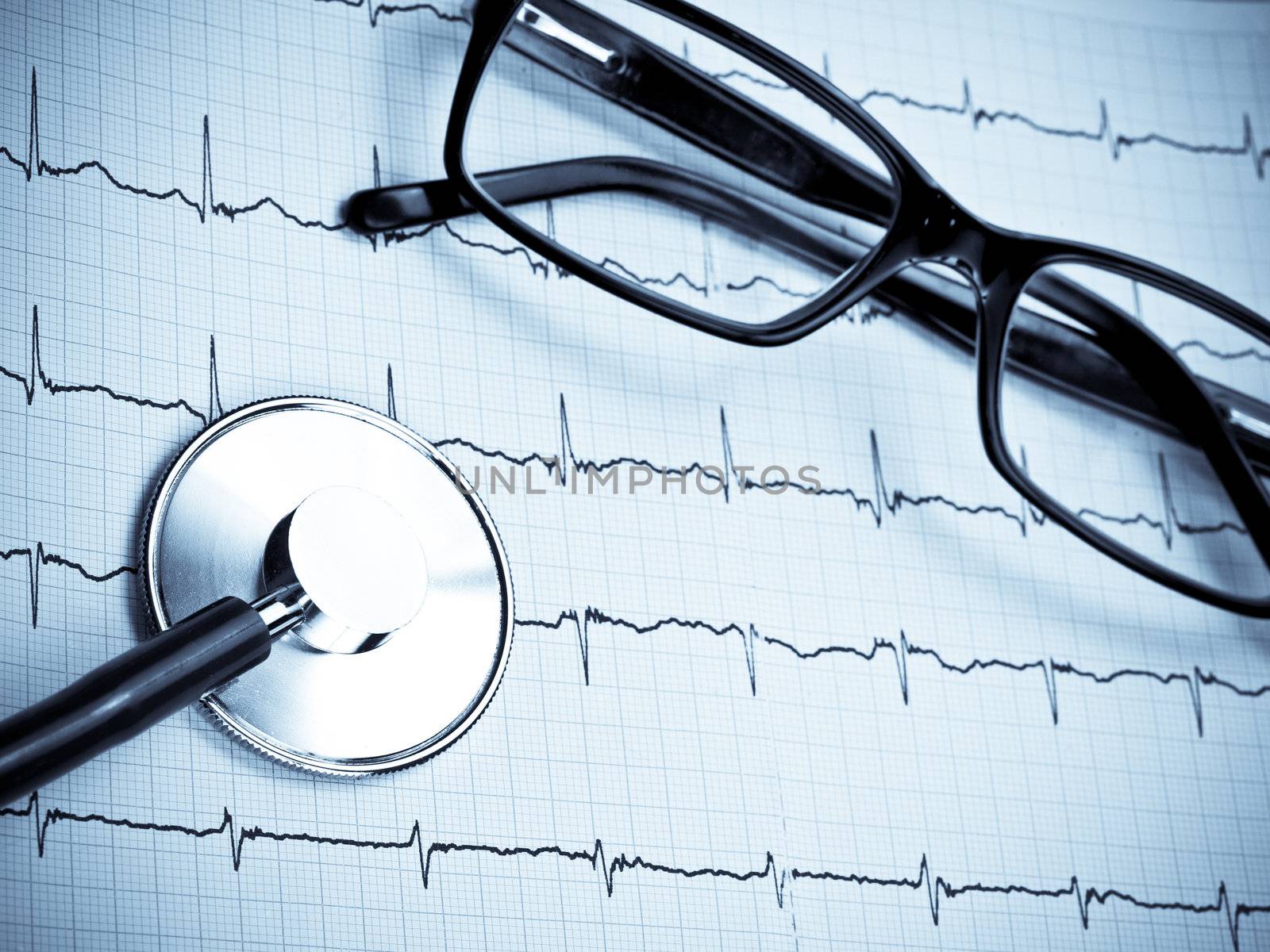 Stethoscope and glasses lying on ECG diagram blue toned