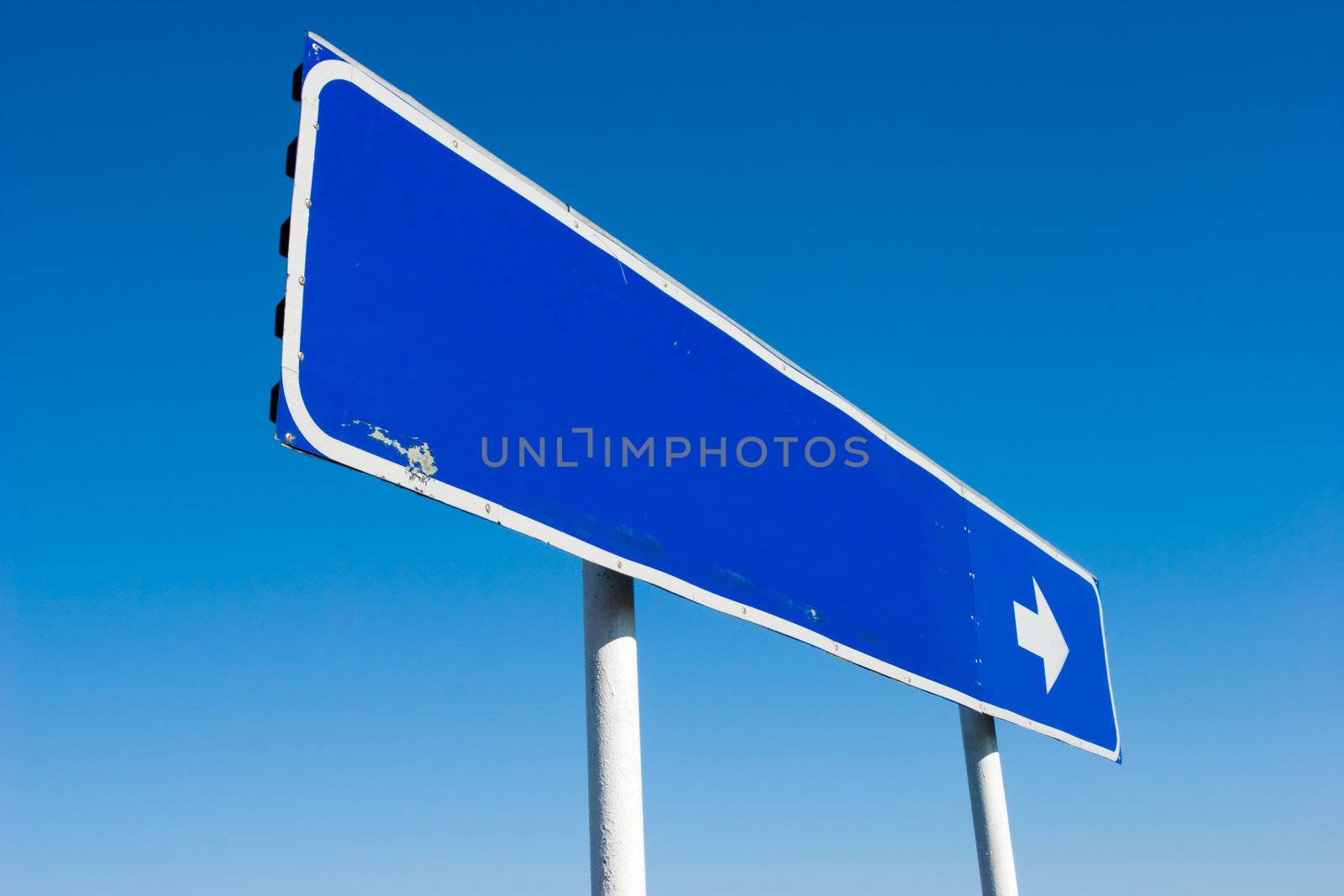 Old grungy blank signpost with direction arrow against blue sky