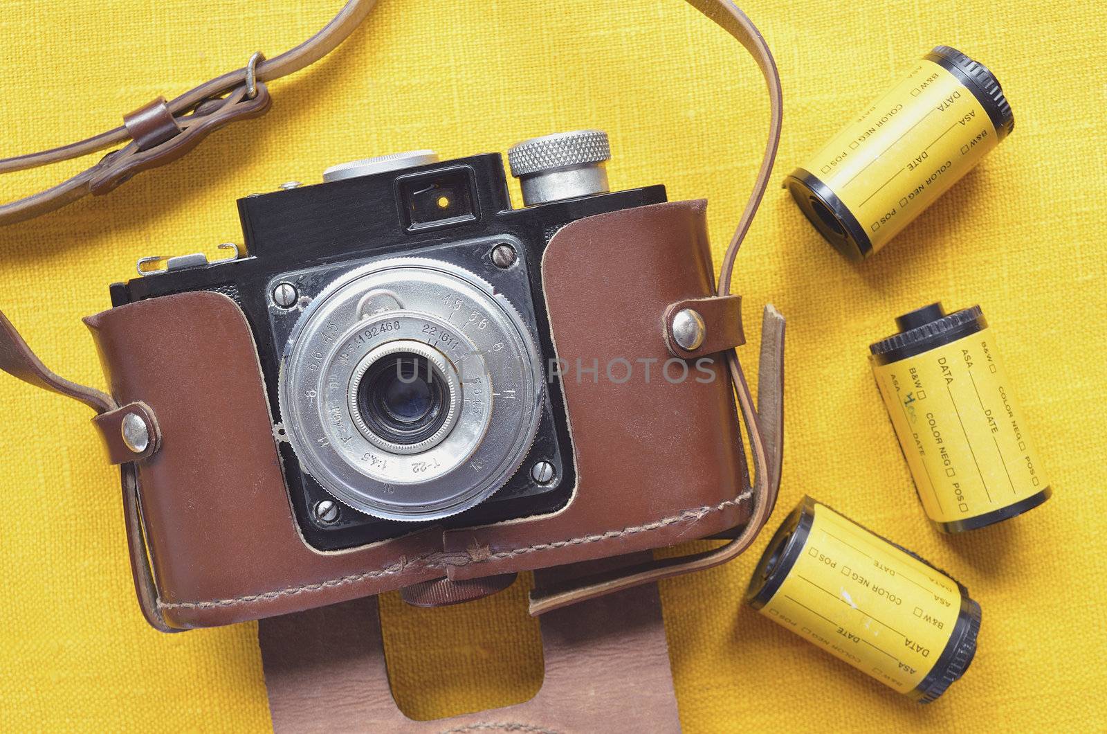 vintage 35mm film camera in leather case with film rolls around; focus on camera body